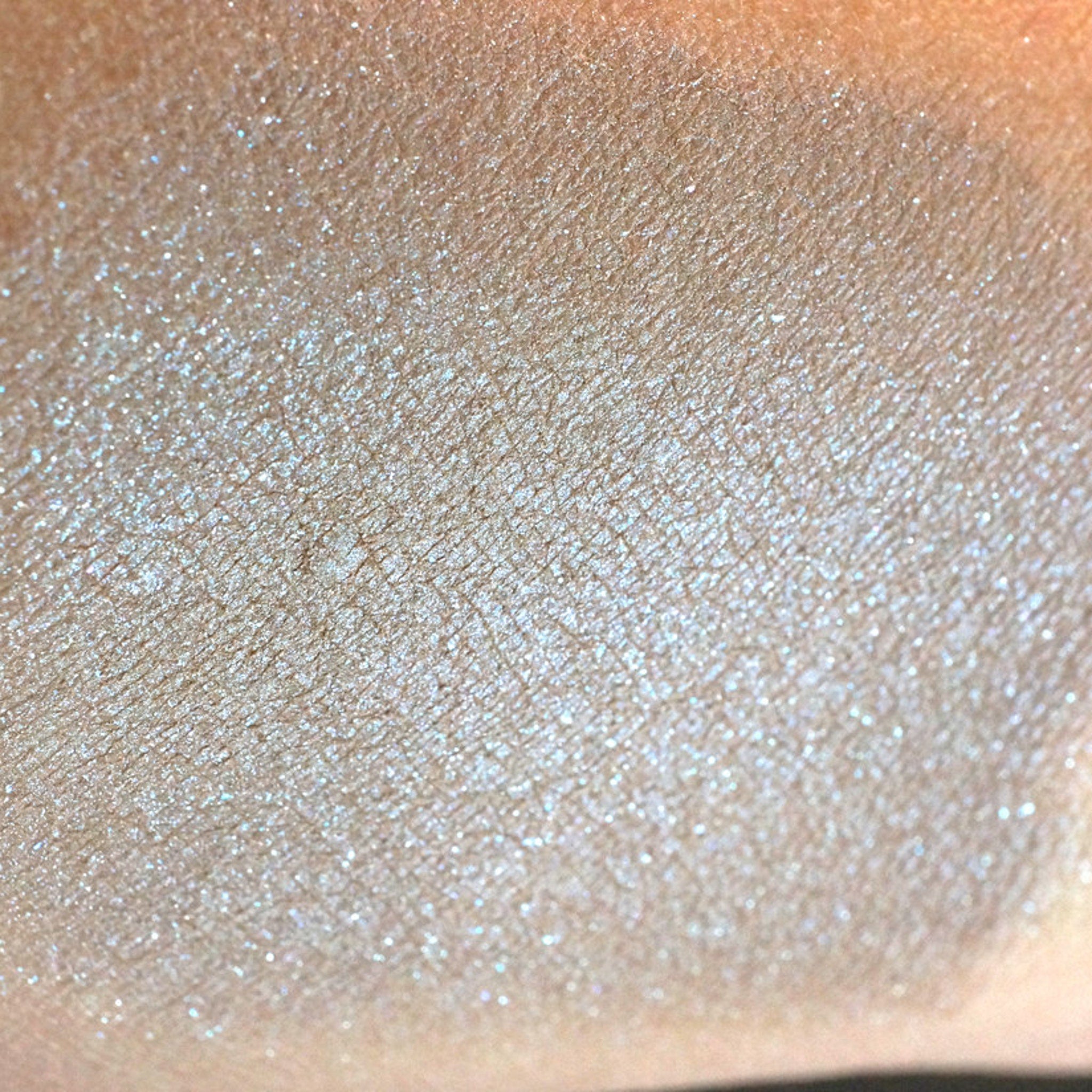 Side view of taupe eyeshadow pan showing beige base with silver and iridescent blue shimmer particles catching light