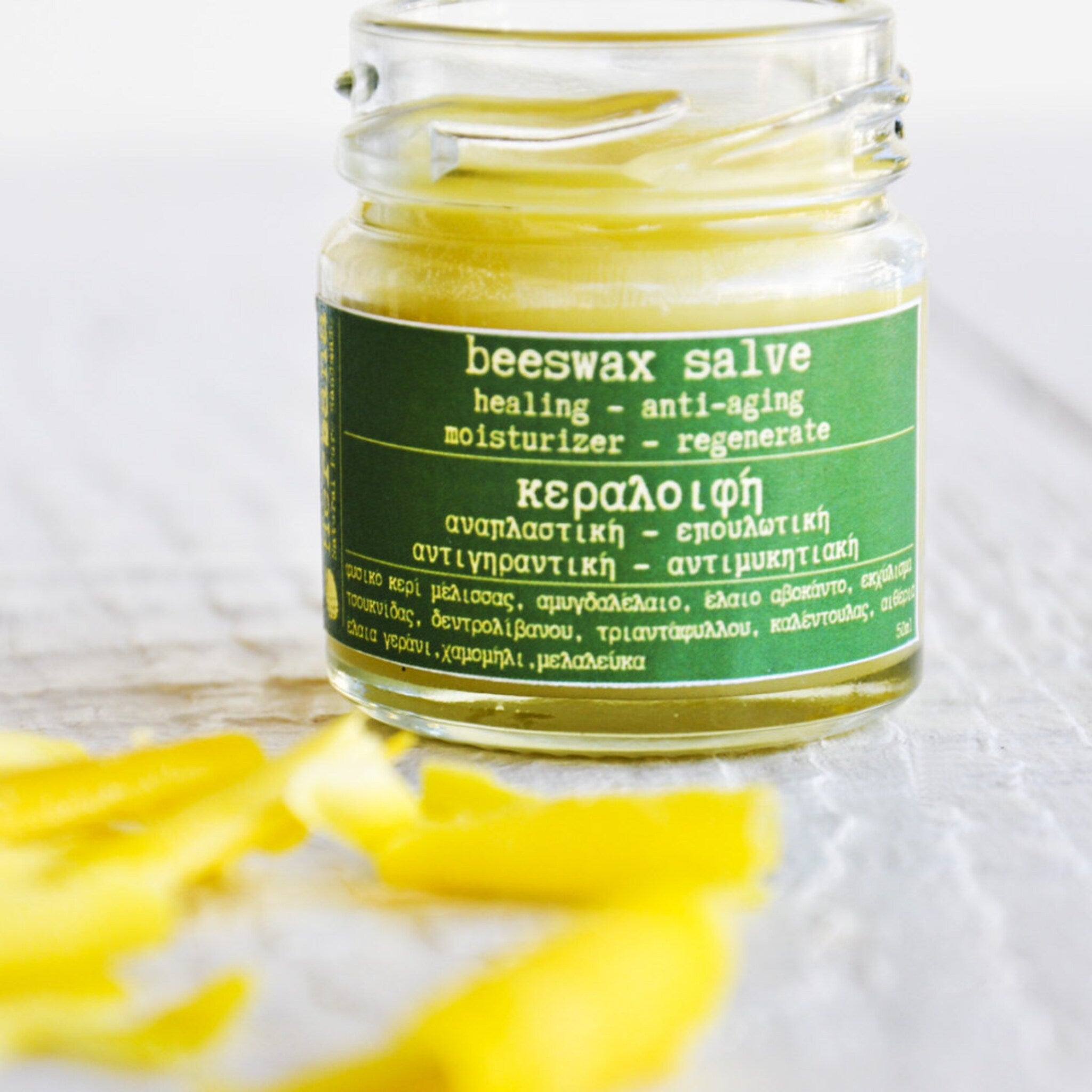 Beeswax salve in a glass jar with green label and yellow contents, on a white surface