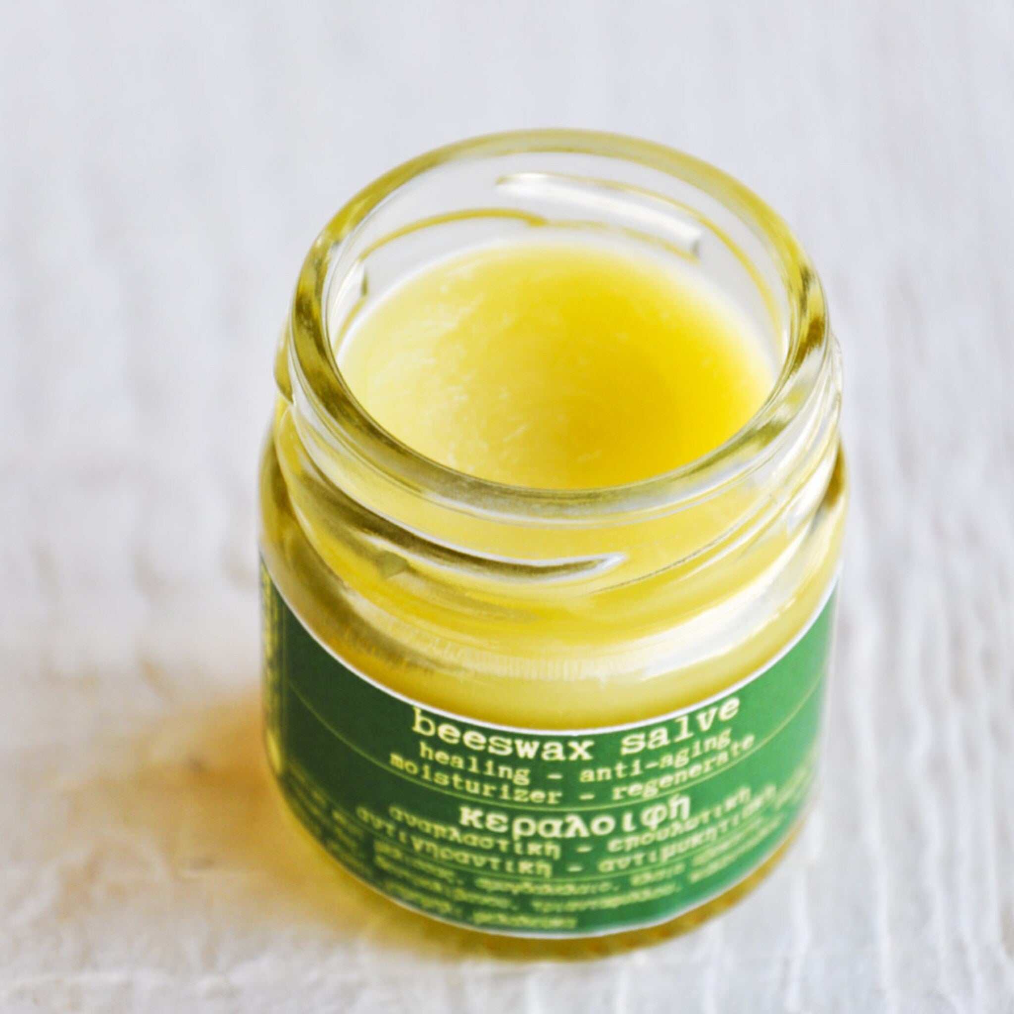 Beeswax salve in a clear glass jar with yellow balm and green label, on white surface