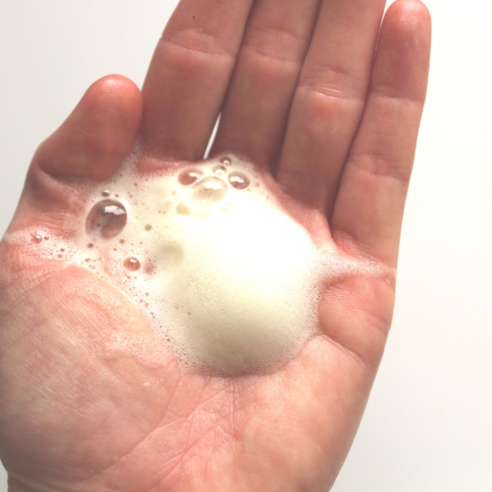 Foam bubbles on skin, white and yellow, in hand, for washing