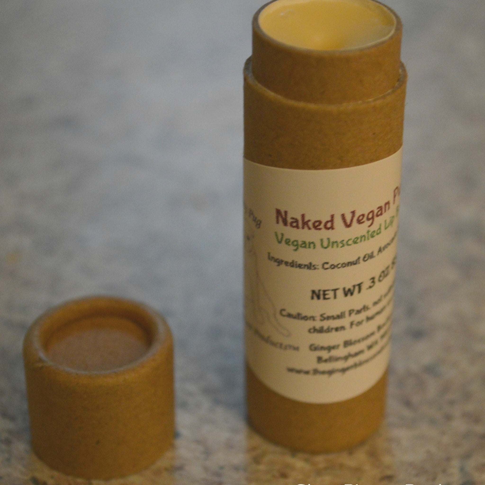 Lip balm in brown cardboard tube with white label, "Naked Vegan" text visible, open lid next to it