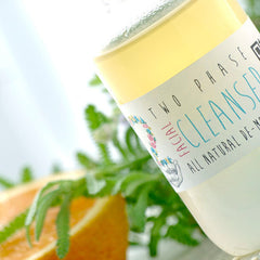 Facial cleanser bottle with yellow and white liquid, label with floral design, and green foliage nearby