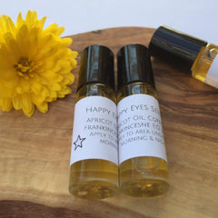 Eye serum bottles with black caps and white labels on a wooden surface next to a yellow flower