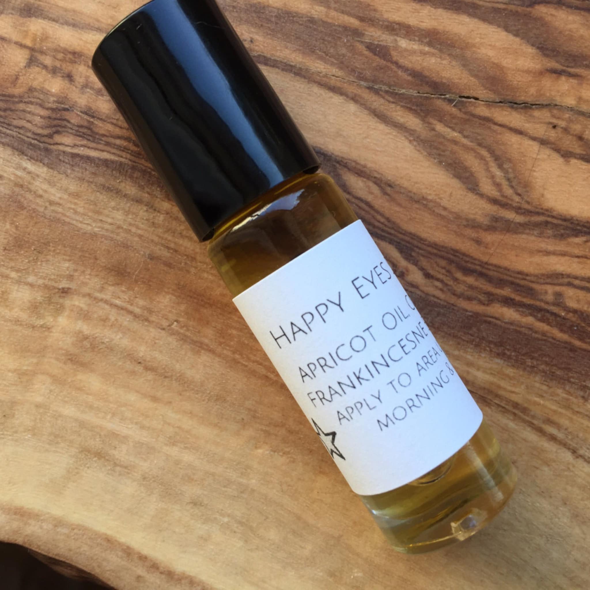 Eye oil roll-on bottle with black cap, clear glass, and white label on wood surface