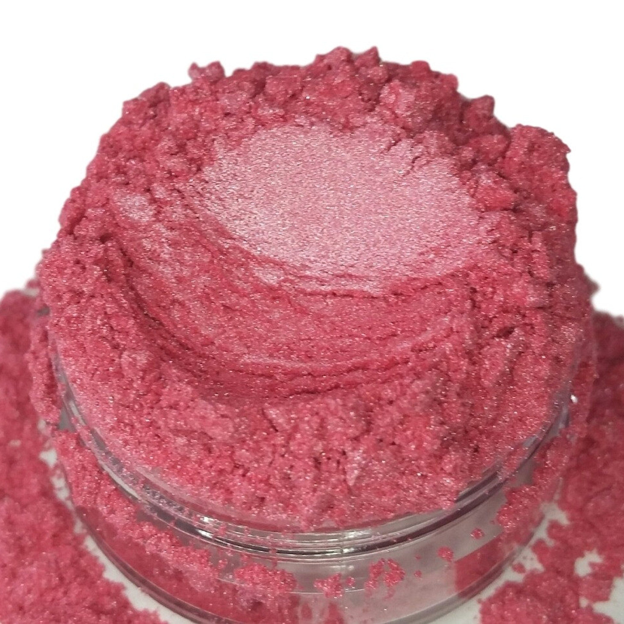 Pink cosmetic powder with glittery texture in a clear jar, close-up view
