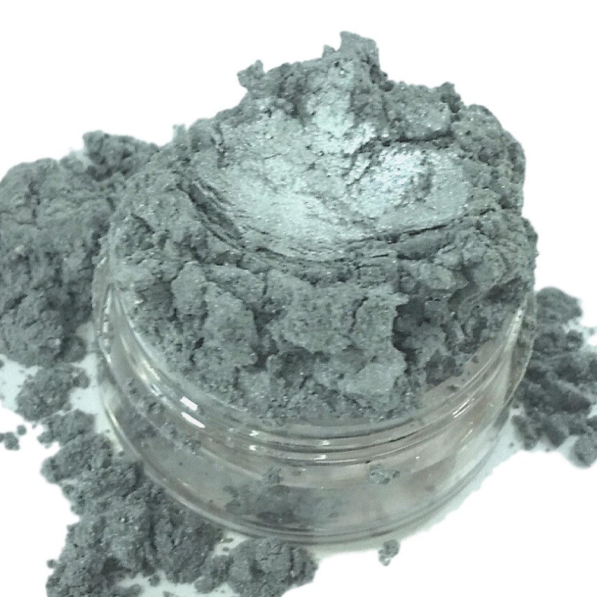 Gray eyeshadow powder in a clear jar, with a metallic finish and loose texture.