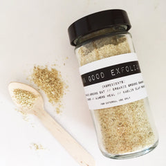 Exfoliating powder in glass jar with black lid, light brown granules, and wooden spoon