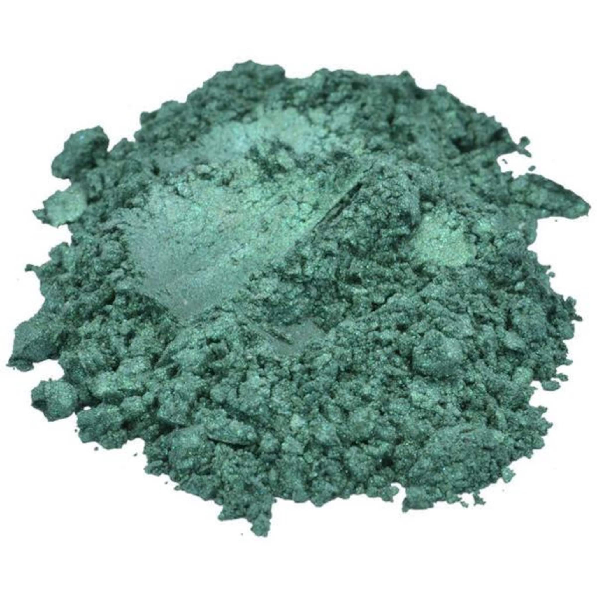 Small glass jar with black lid containing vibrant aqua green mica pigment powder for eyeshadow.