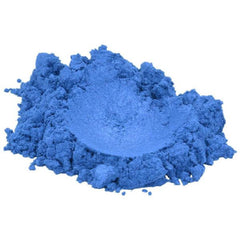 Close-up of sapphire blue mica pigment powder spilling from jar onto reflective silver surface