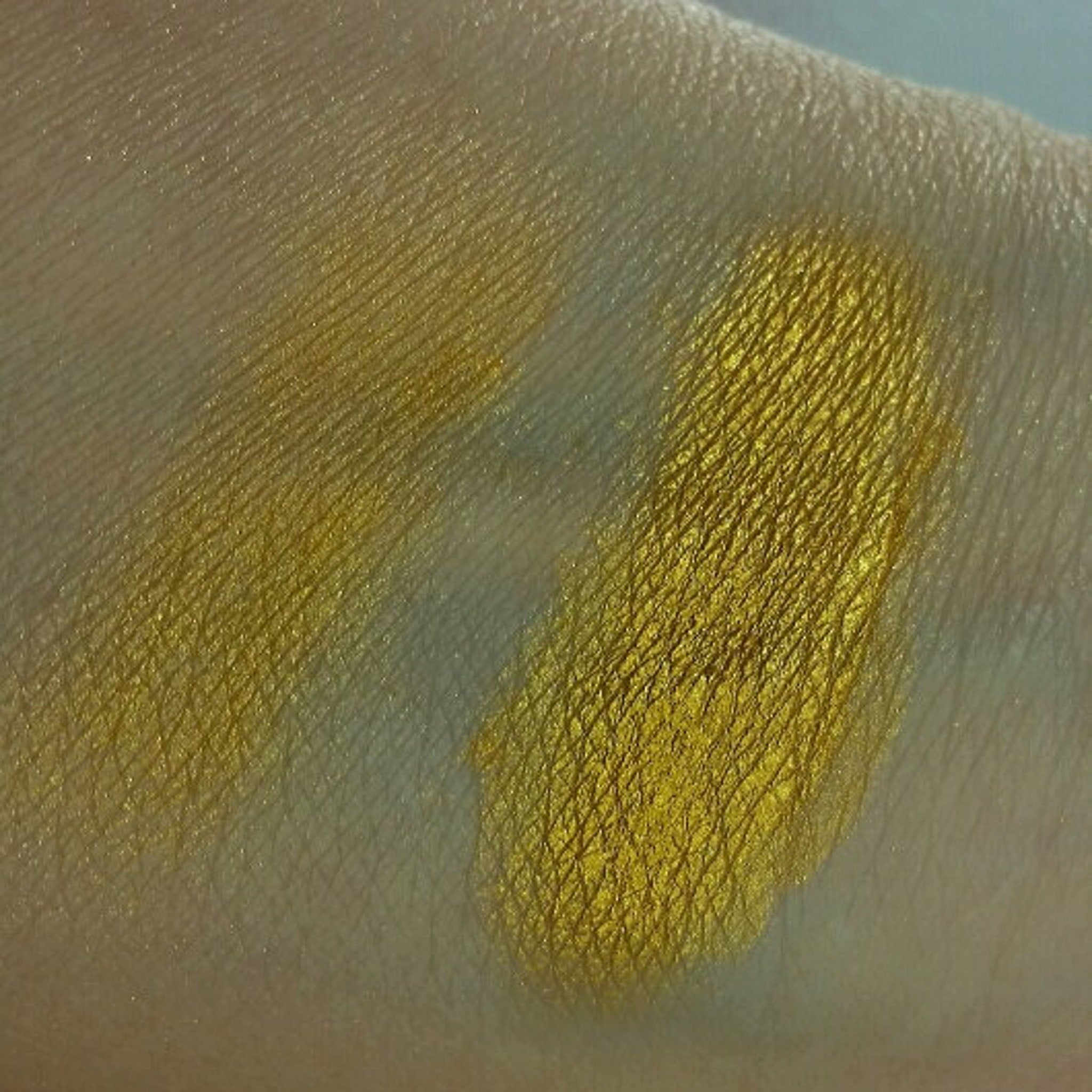 Yellow eyeshadow swatch on skin, metallic gold color, textured appearance, applied on arm