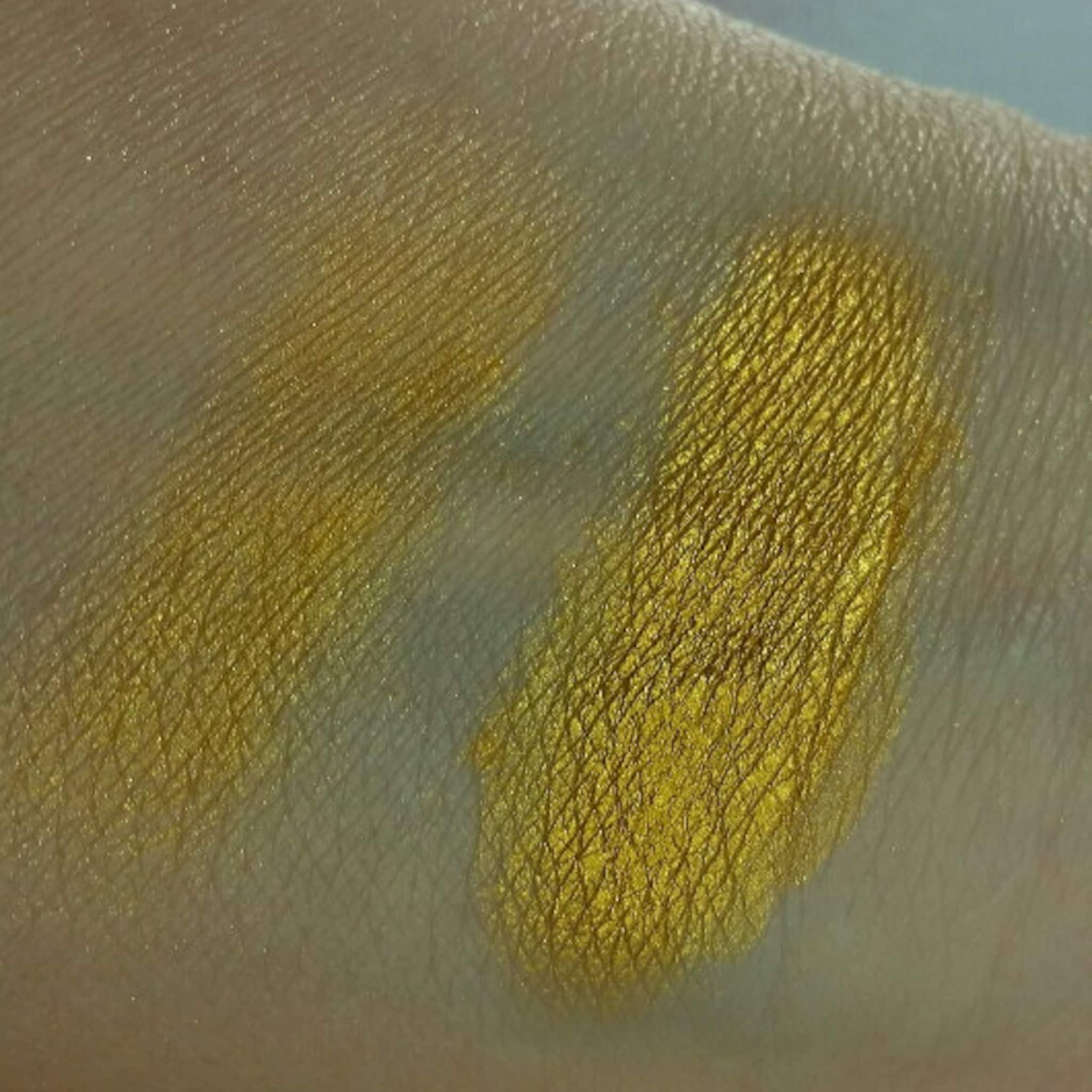 Close-up of fingertips applying iridescent blue-gold eyeshadow with metallic shimmer to eyelid