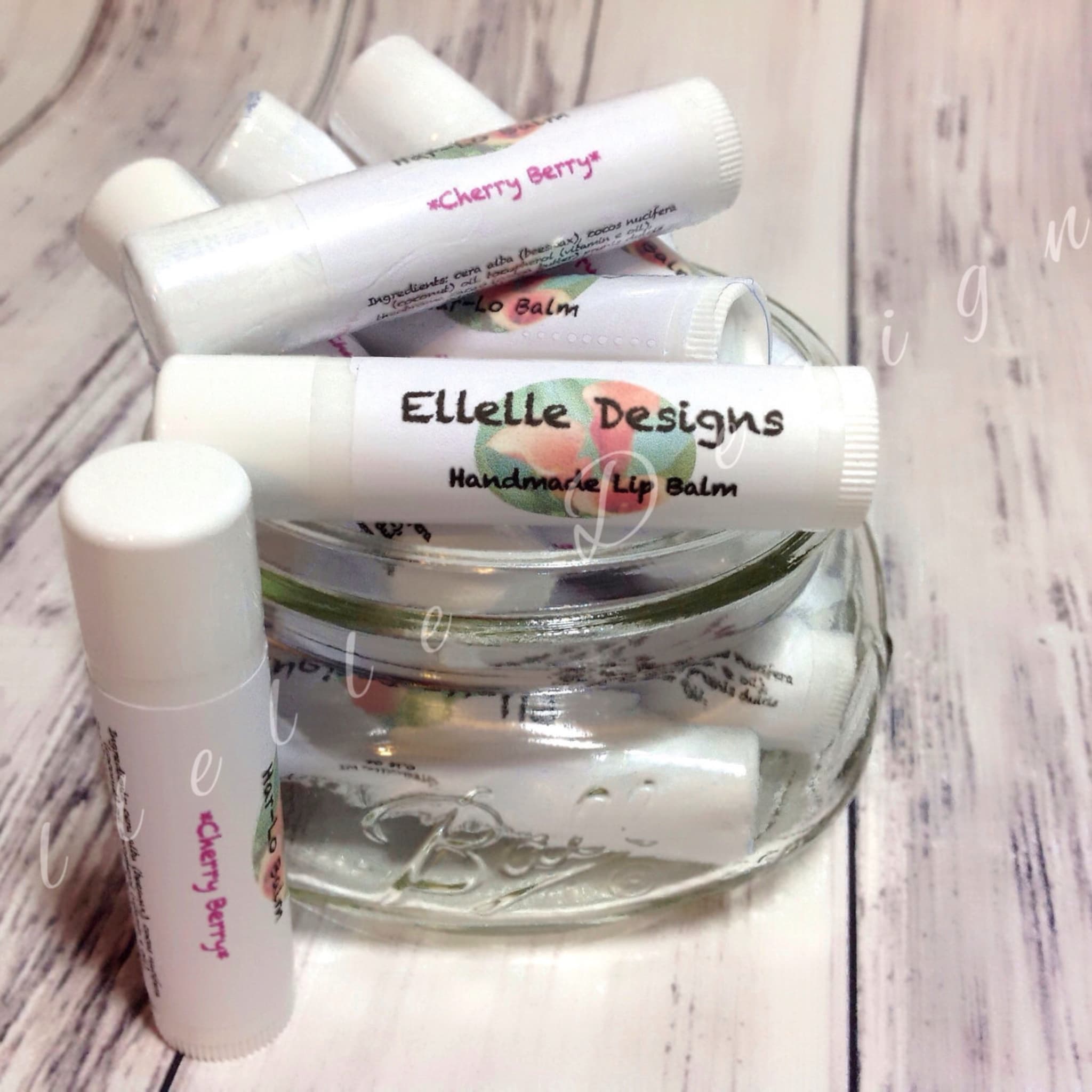 Lip balm tubes, white with pink text, in a glass jar, Ellelle Designs brand name visible