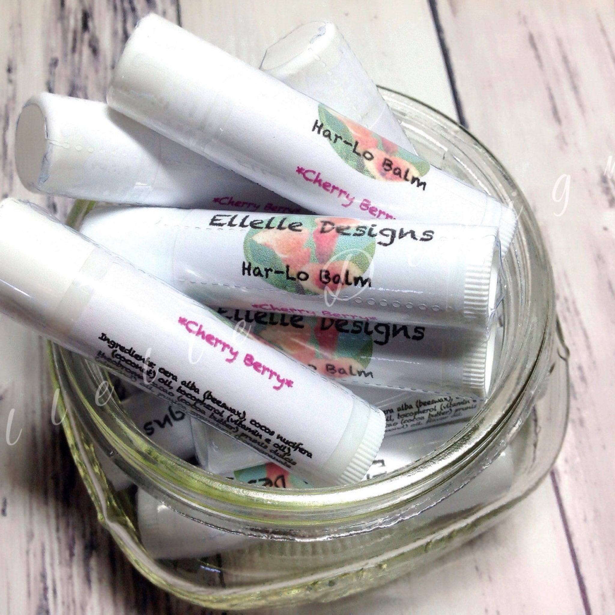 Lip balm tubes, white with printed labels, inside a glass jar, "Cherry Berry" text visible