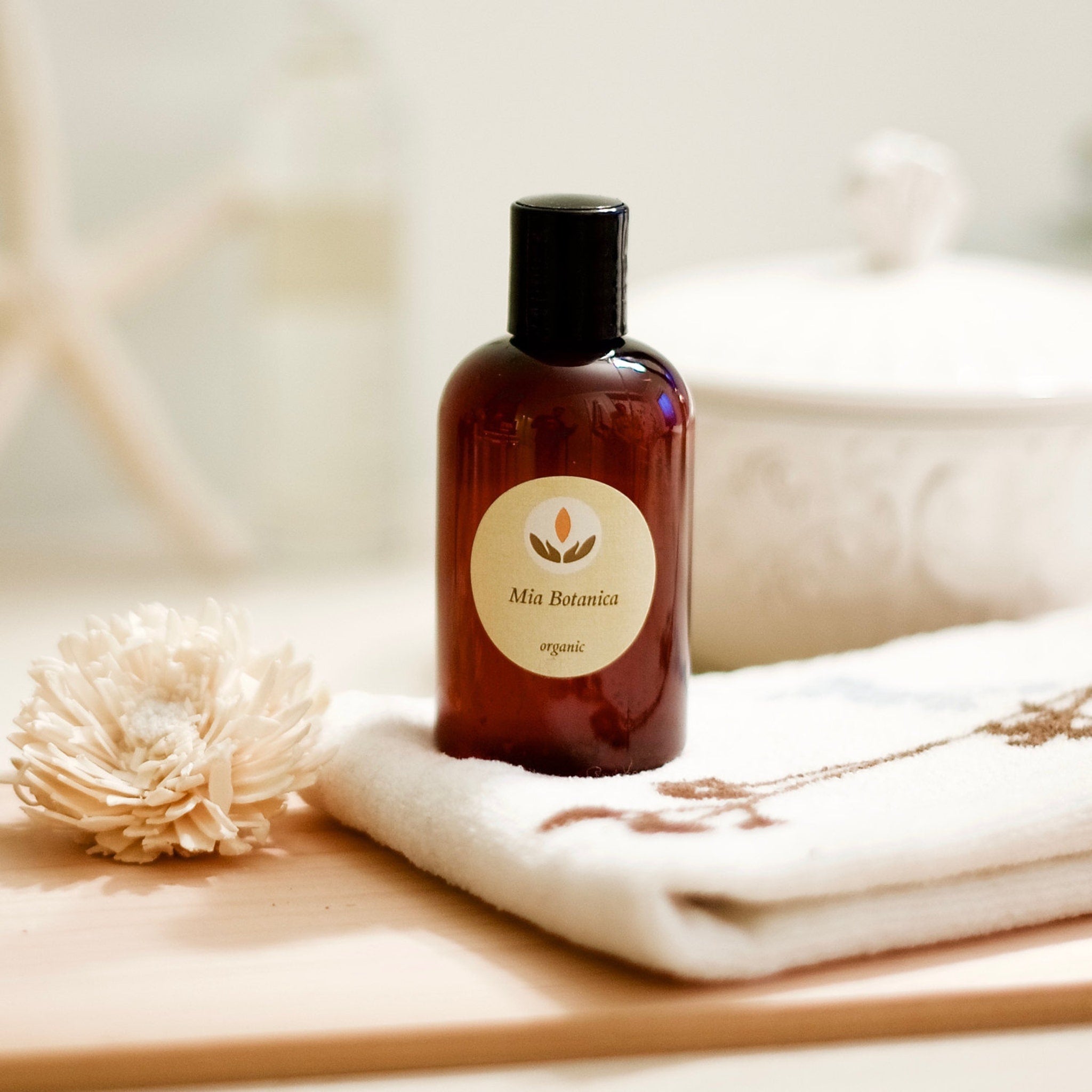 Brown bottle with black cap, Mia Botanica label, on white towel with flower