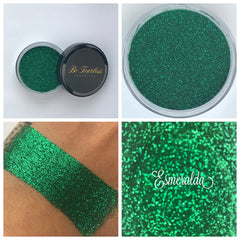 Close-up of Esmeralda loose cosmetic glitter in a glass jar with gold lid, showcasing vibrant emerald green shimmer particles.