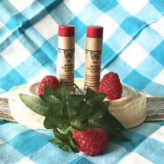 Lip balm tubes with red tops and brown paper labels, on blue and white plaid background