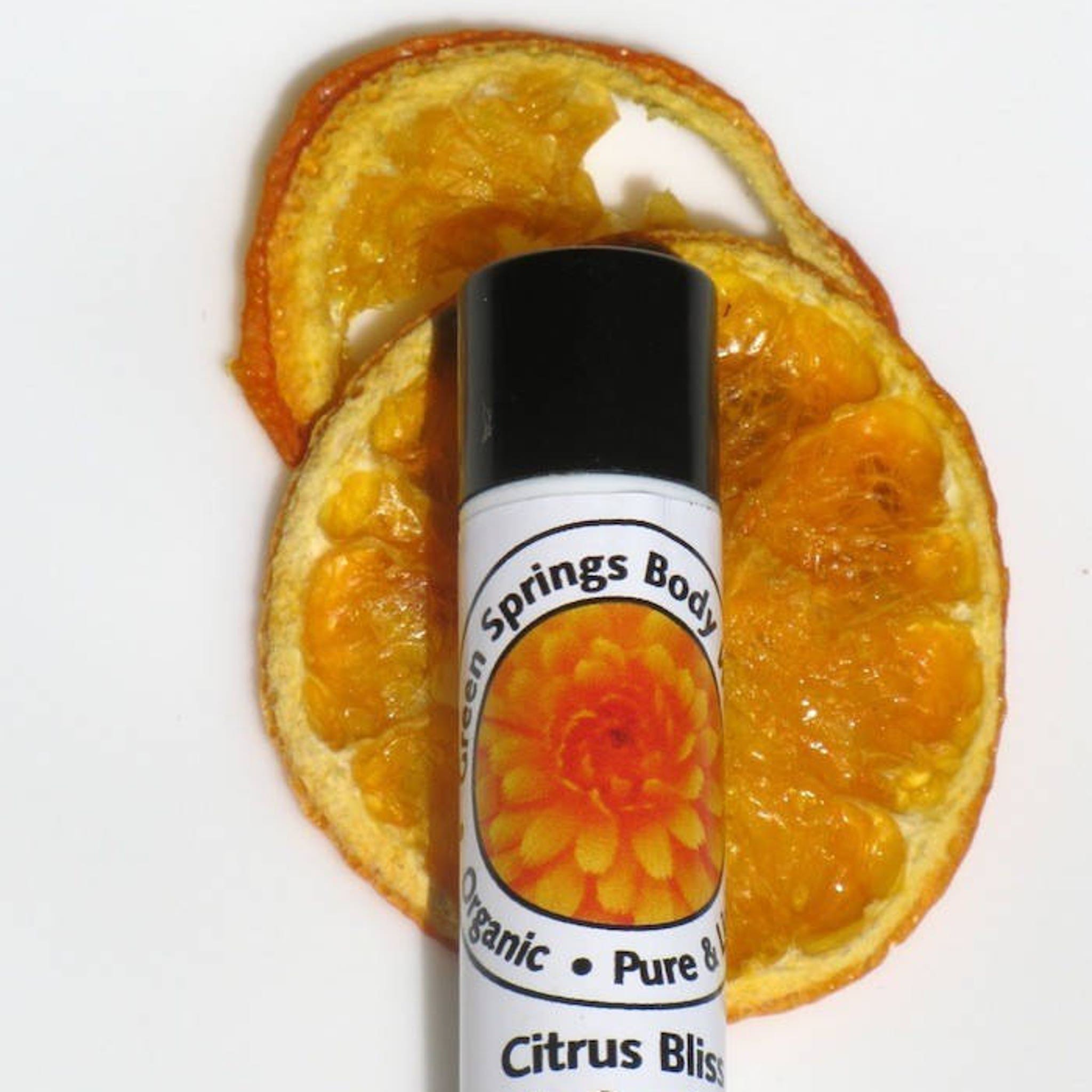 Lip balm with black cap, white label, and orange fruit slices on white background
