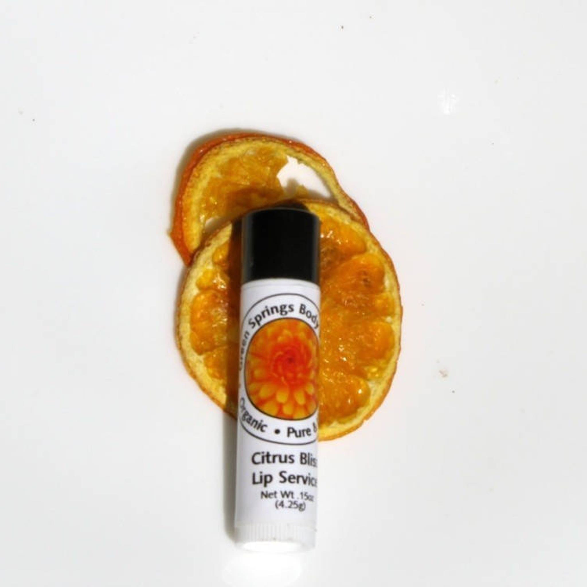 Lip balm with white tube, black cap, and orange dried fruit slices on white surface