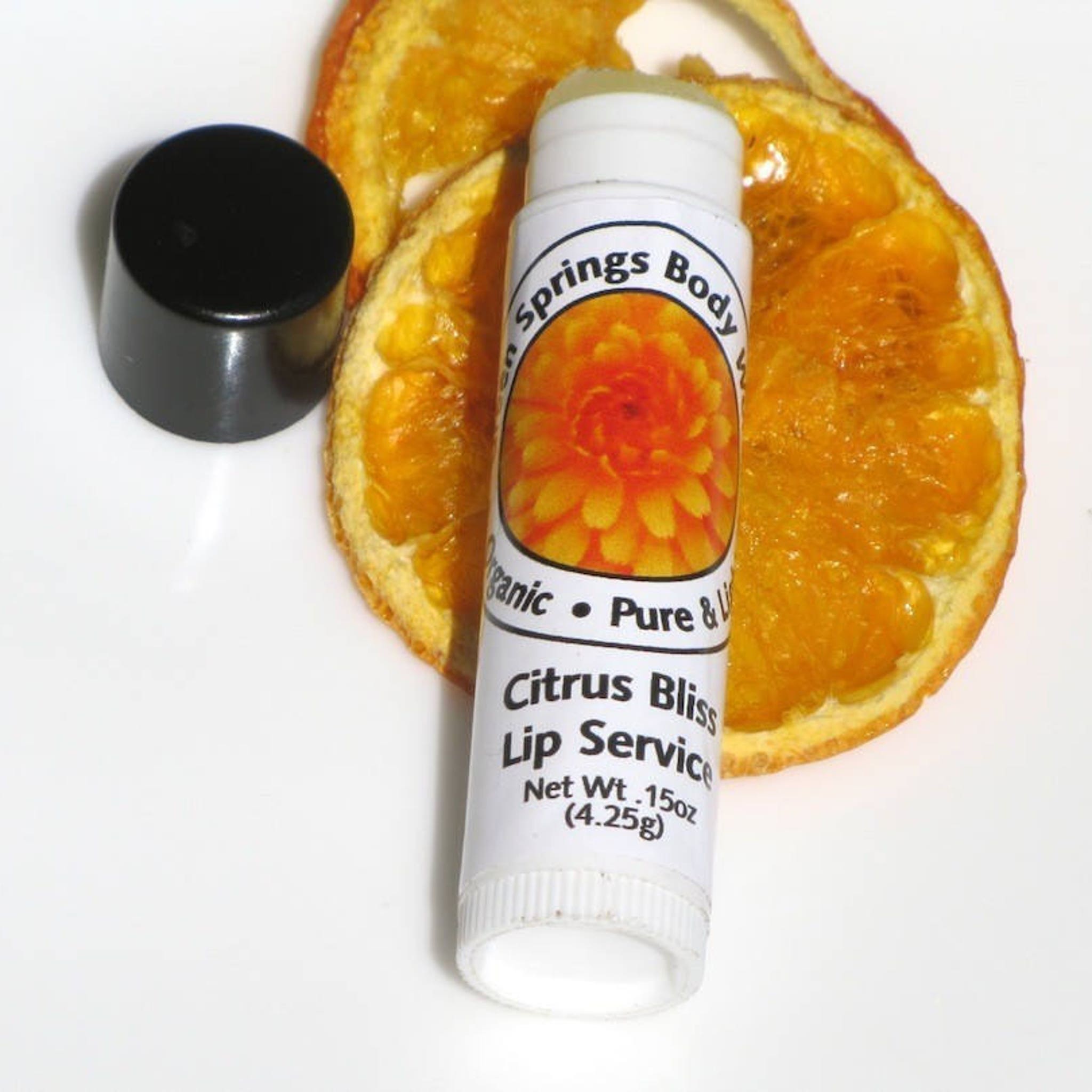Lip balm tube with white label, black cap, and orange slices, "Citrus Bliss" label visible