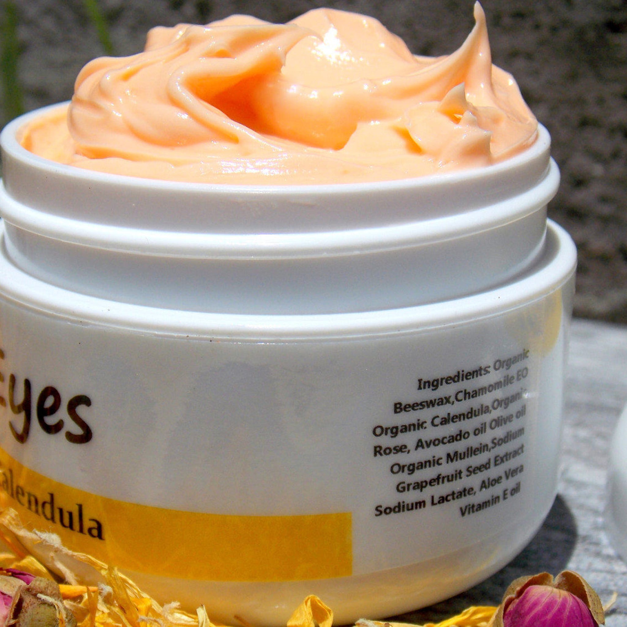 Eye cream in white jar with peach cream and "yes" text, yellow label, and rose petals