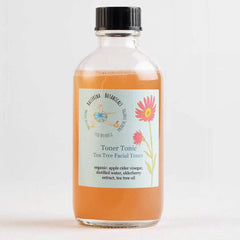 Facial toner bottle with orange liquid, clear glass, and black cap, Ballerina Botanicals label visible
