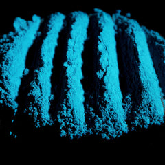 Side view of matte teal loose eyeshadow in glass jar with gold lid, showcasing rich peacock turquoise pigment texture