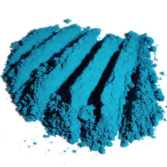 Hand applying matte teal loose eyeshadow with brush, creating a swatch on skin to show dark peacock turquoise pigment.