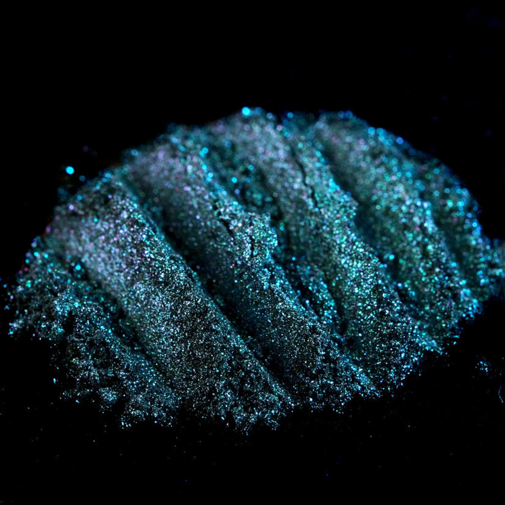 Side view of iridescent teal eyeshadow pan with colorshifting glitter, showcasing mermaid-inspired turquoise hues.