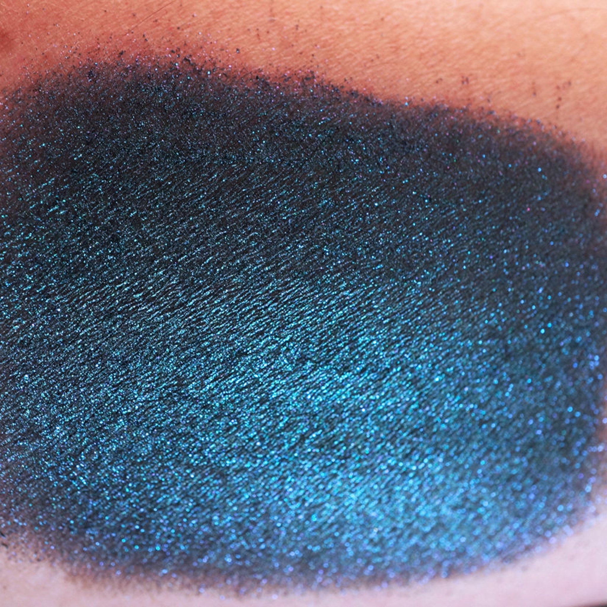 Side view of iridescent teal eyeshadow pan showing colorshifting glitter in mermaid-inspired vegan makeup