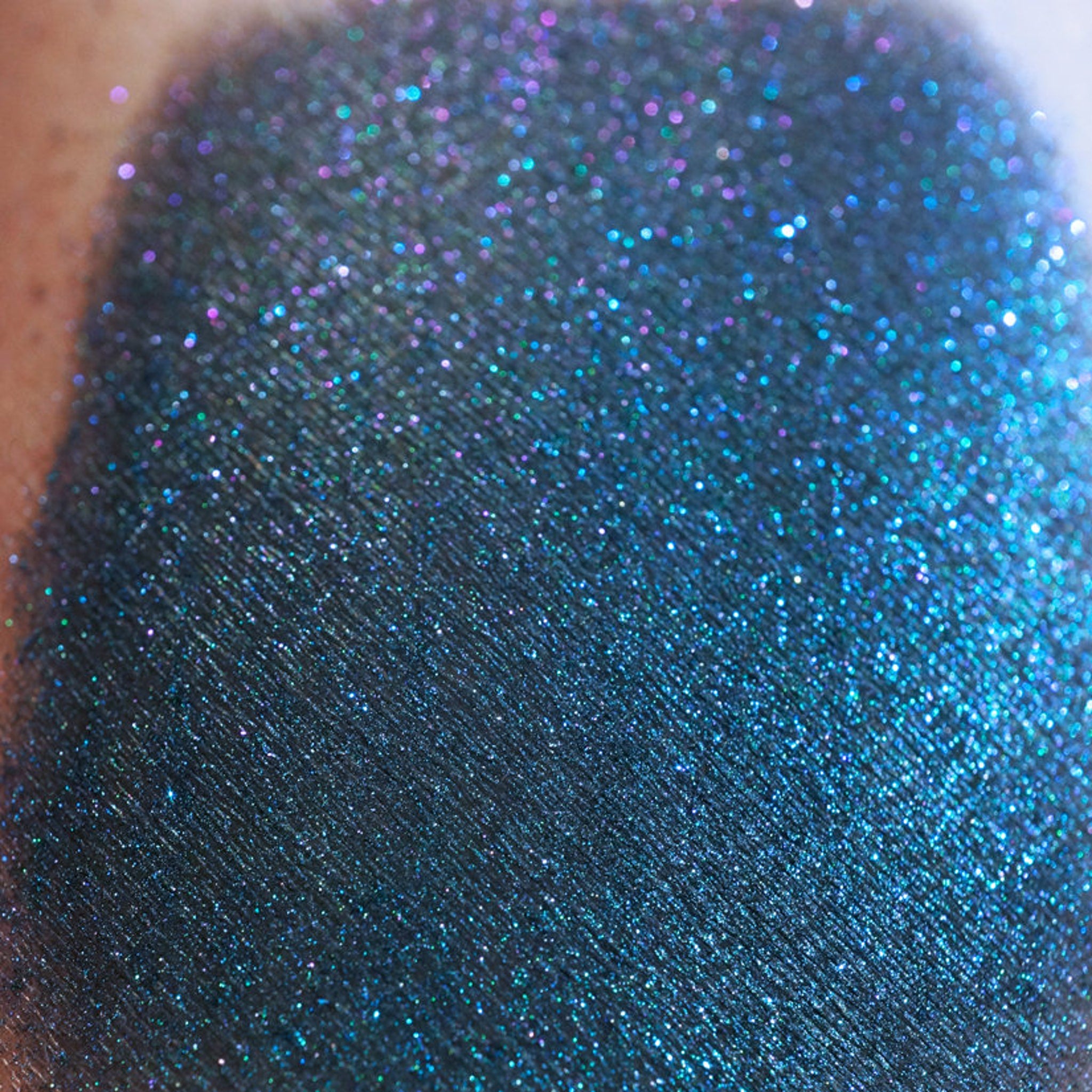 Side angle view of iridescent teal eyeshadow pan with colorshifting glitter in mermaid-inspired packaging