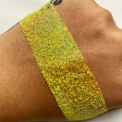 Yellow glitter swatch on skin, showing texture and color variation, for cosmetic use