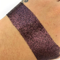 Close-up of mocha brown loose glitter eye shadow with shimmering particles in a glass jar