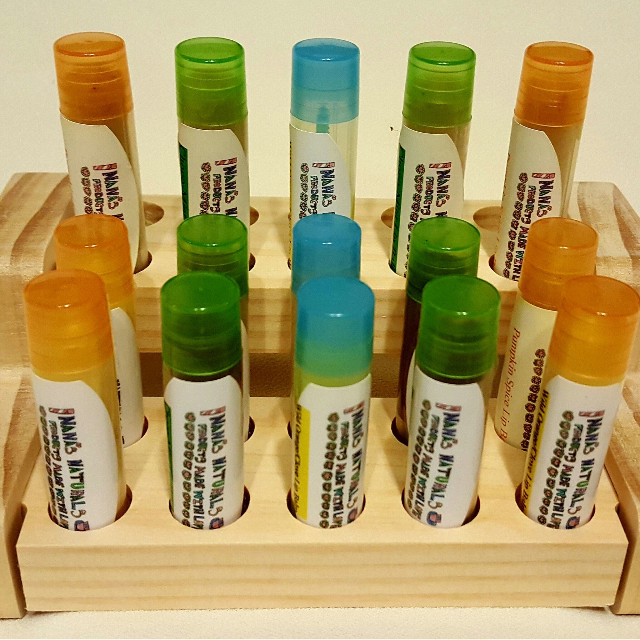 Lip balm tubes with orange, green, and blue caps, white labels, and wooden display stand, NANAS brand