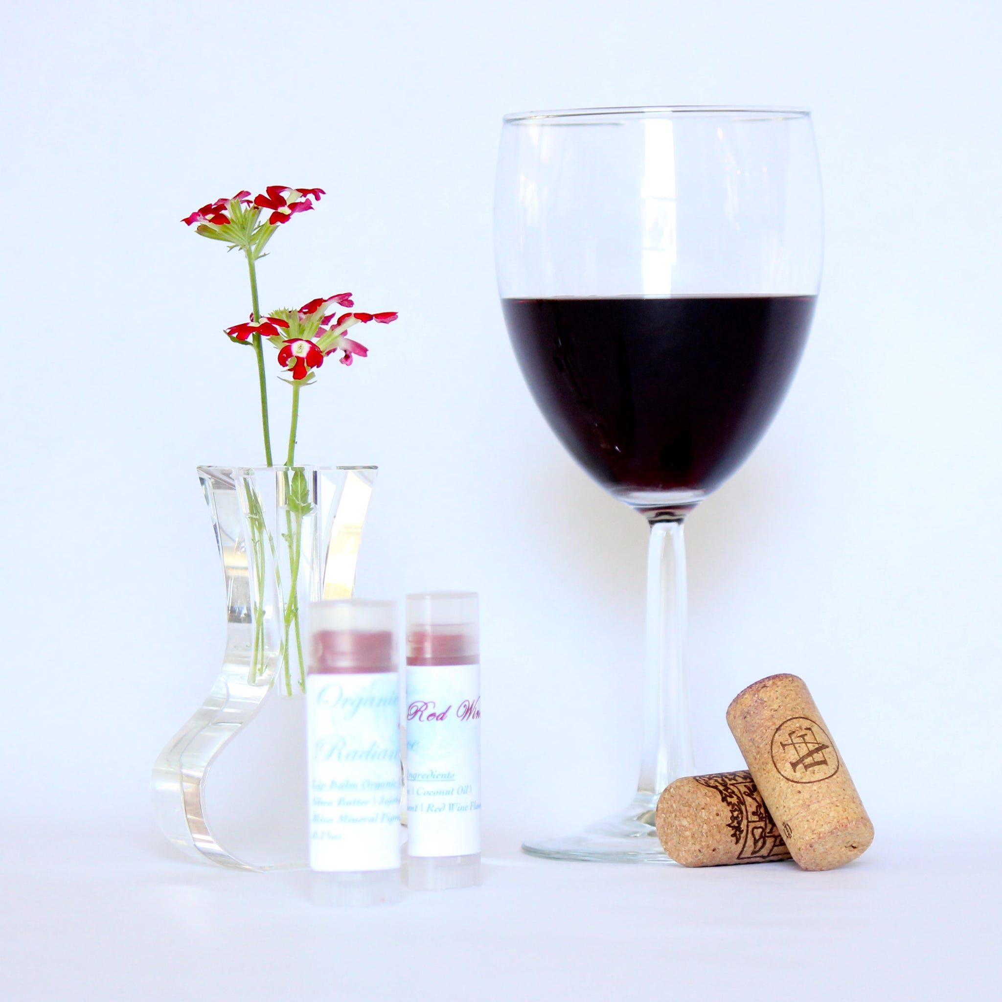 Lip balm tubes with white labels, clear caps, and red tint next to wine glass