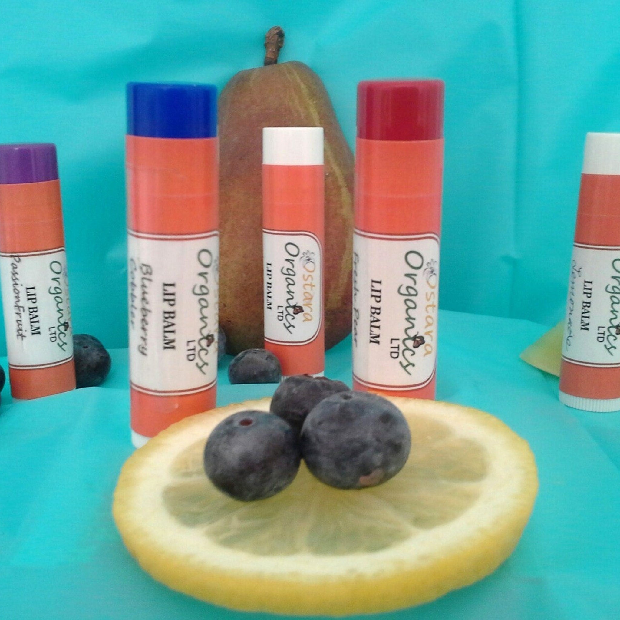 Lip balm tubes with orange, white label, and colored caps, with blueberries and lemon slice