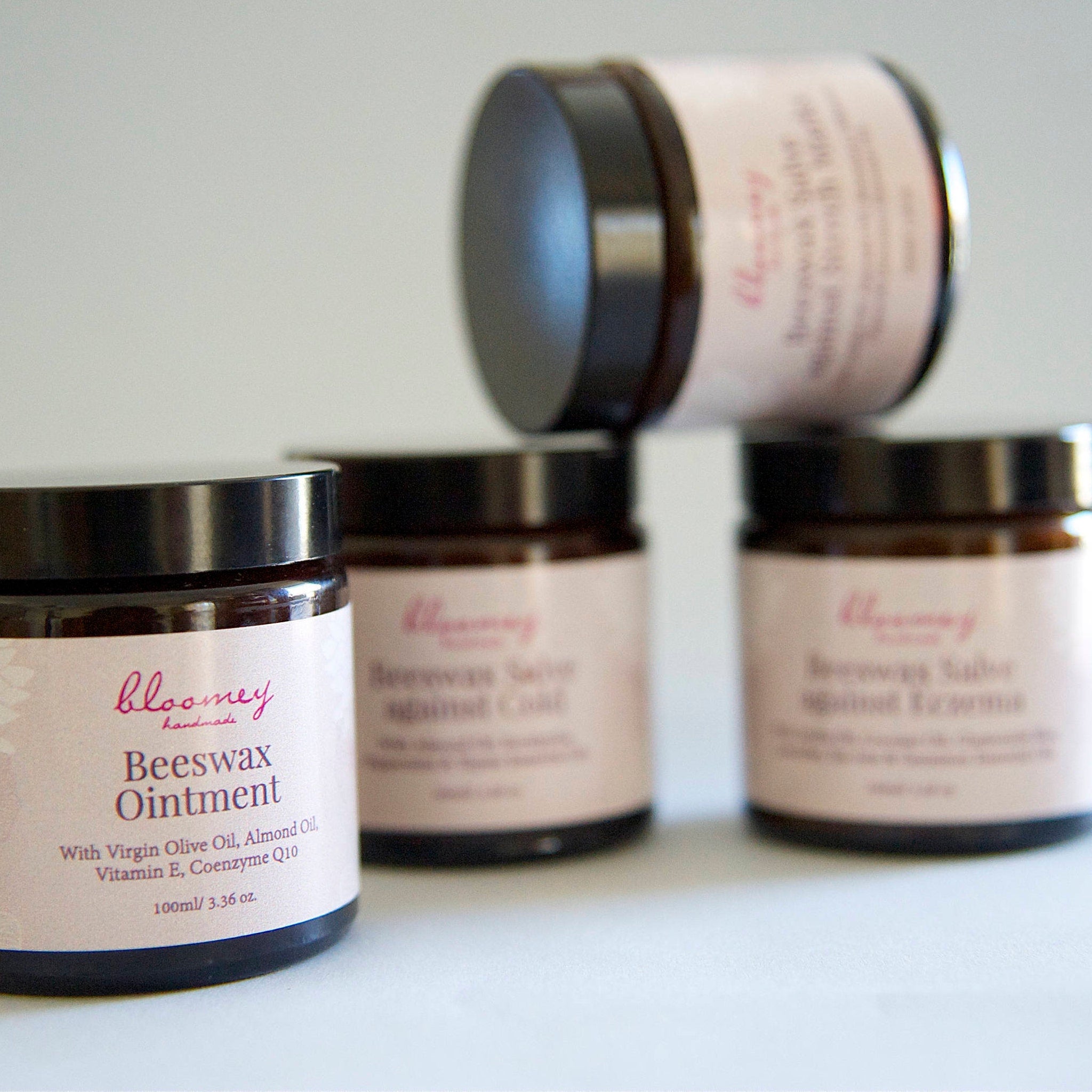 Beeswax ointment jars with black lids and pink labels, bloomey handmade brand visible