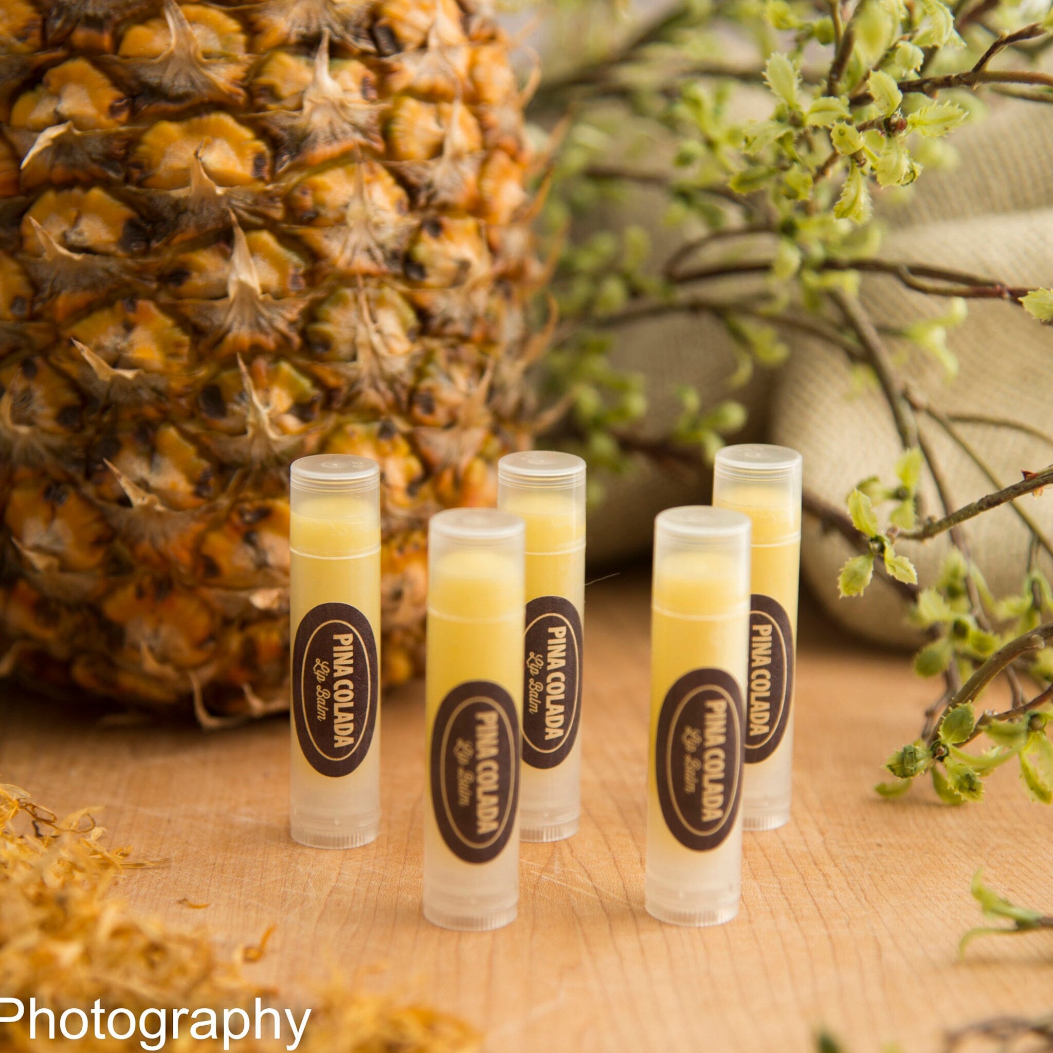 Lip balm tubes with yellow balm, clear plastic, and "Pina Colada" label on wood surface