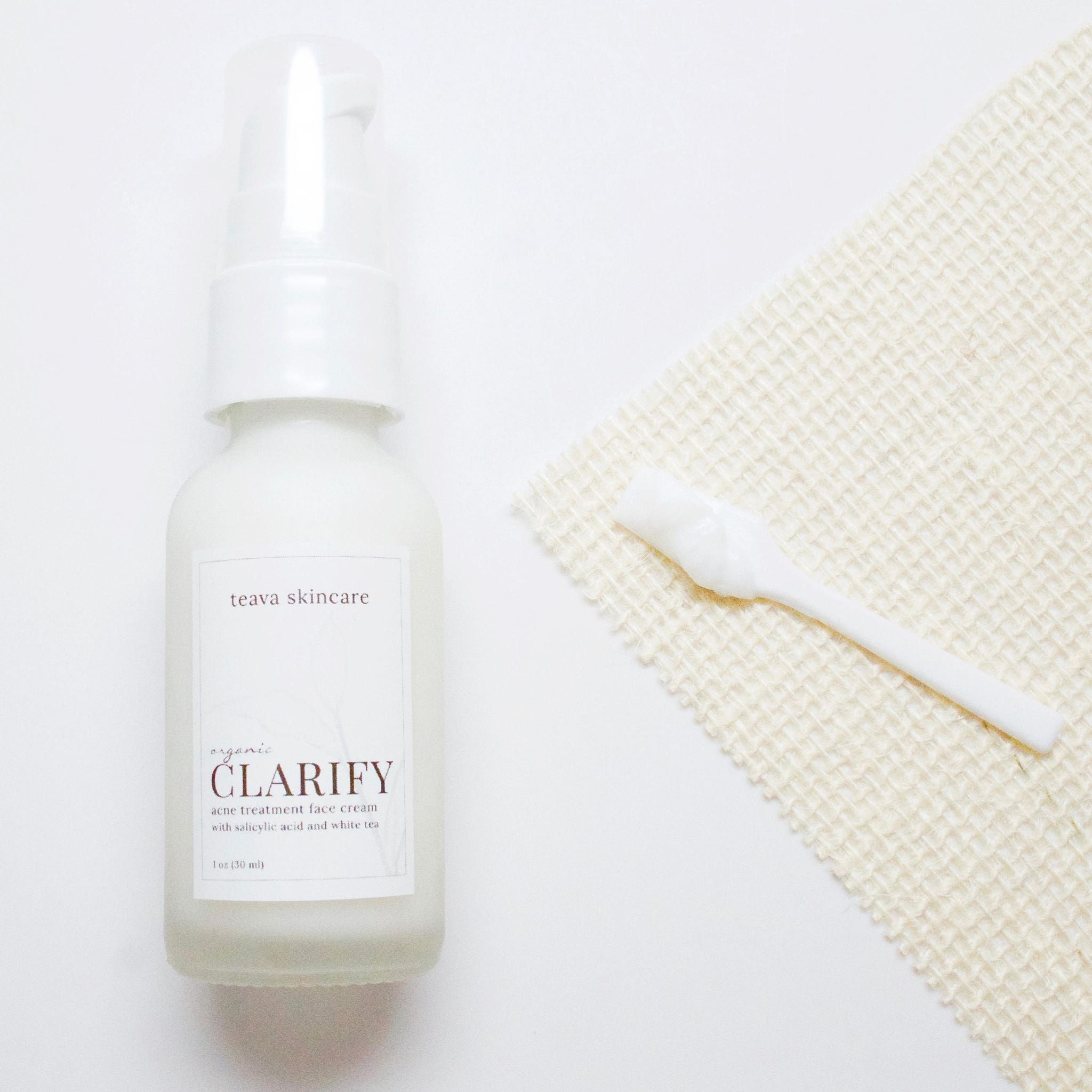 Face cream bottle with white pump, white label, and beige woven cloth beside it