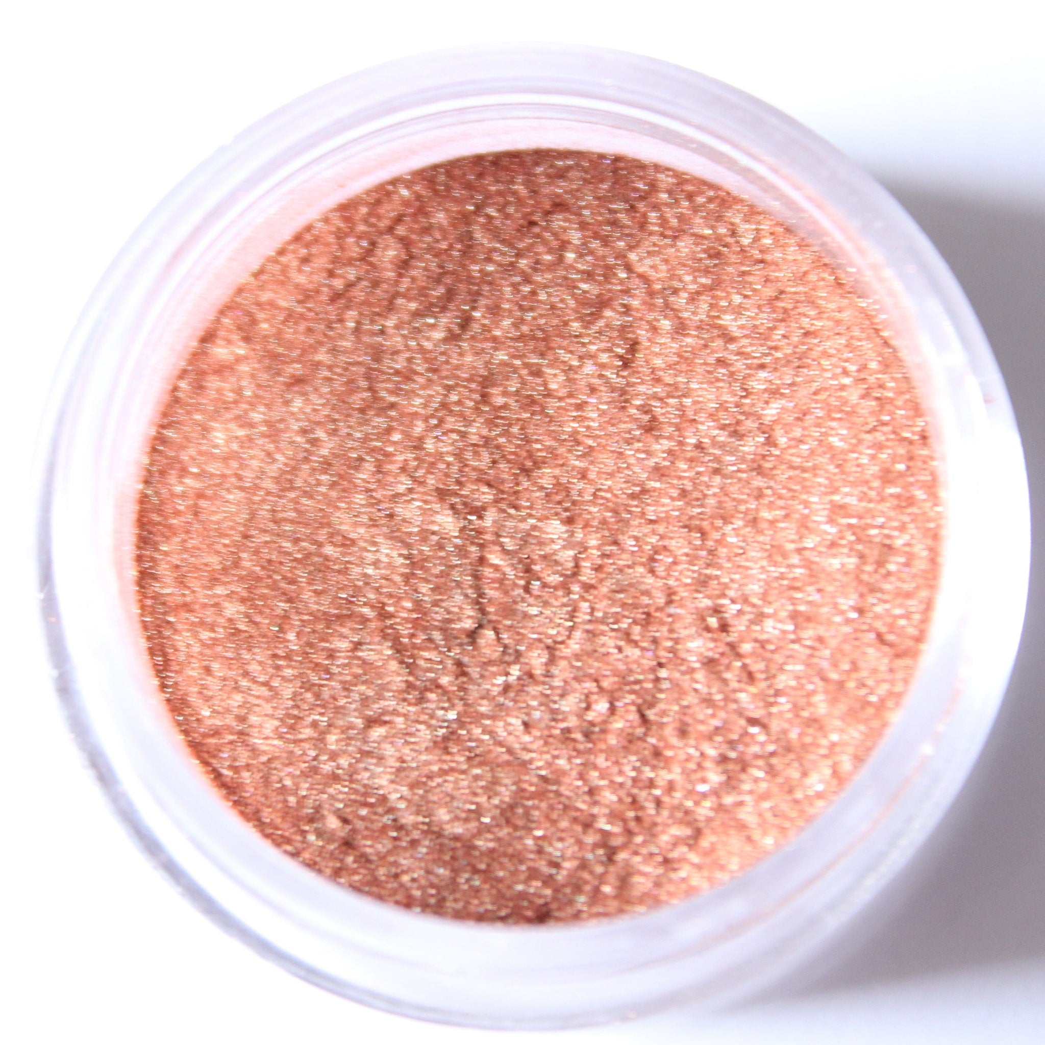 Glass jar of loose mineral eyeshadow in shimmering rose gold with metallic finish, lid removed
