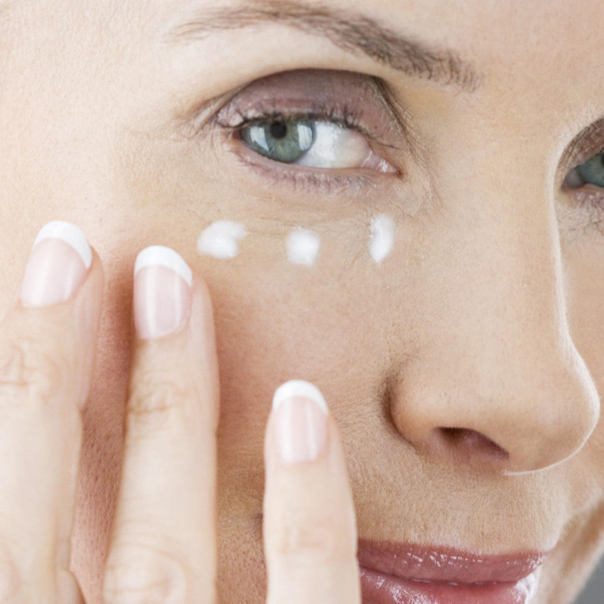 Eye cream application, white cream dots on skin, woman's hand with French manicure