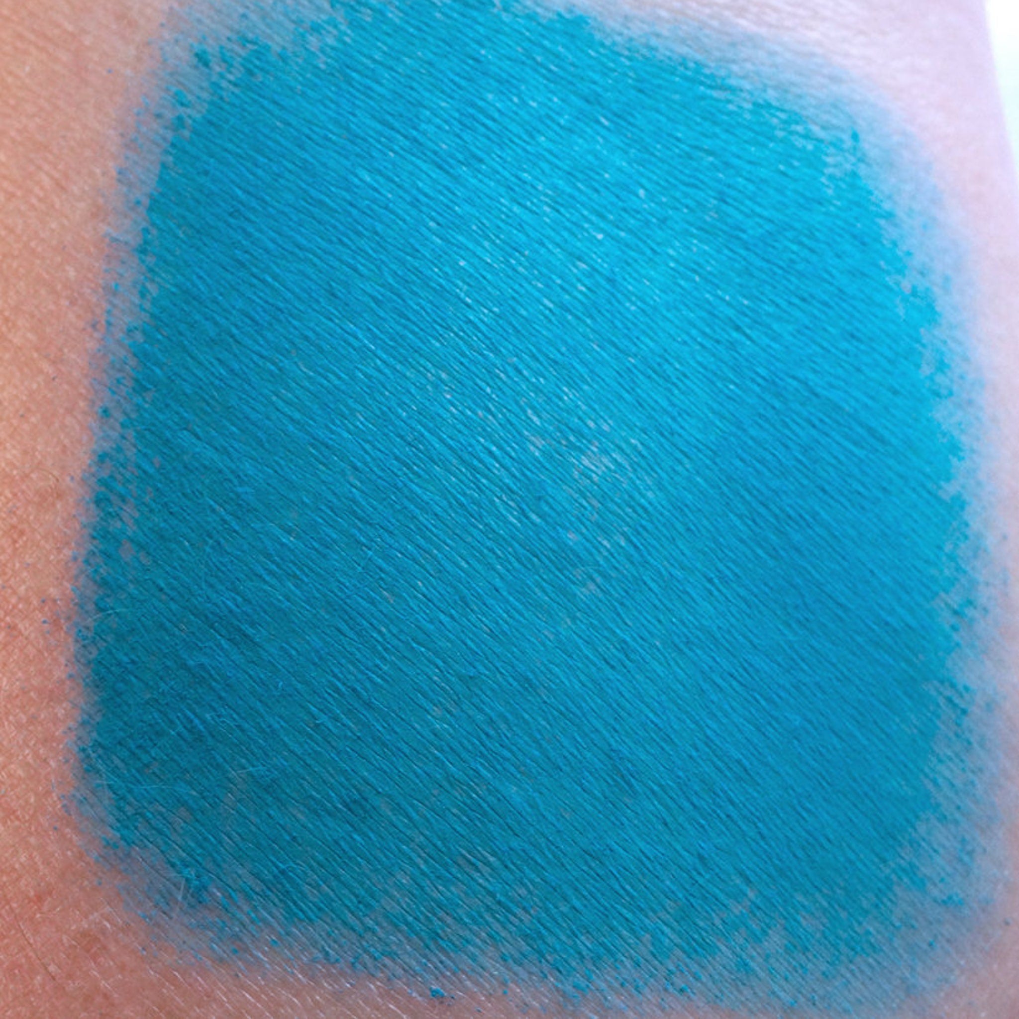 Side view of matte teal loose eyeshadow in dark peacock turquoise, showing fine powder texture in jar