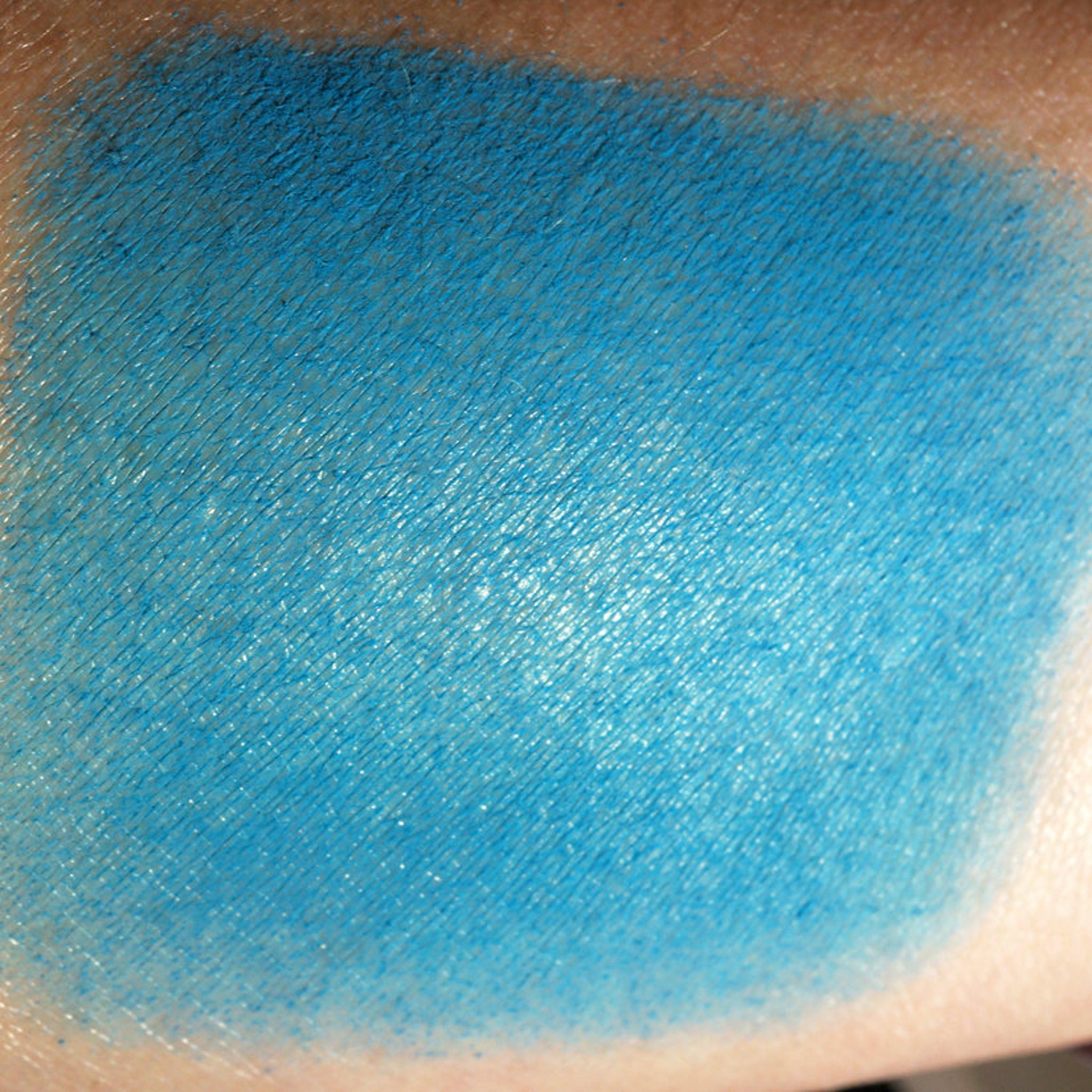 Side view of matte teal loose eyeshadow in dark peacock turquoise, showing fine powder texture in open jar