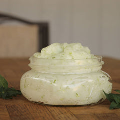 Body scrub in a clear glass jar with light green and white texture on wooden table