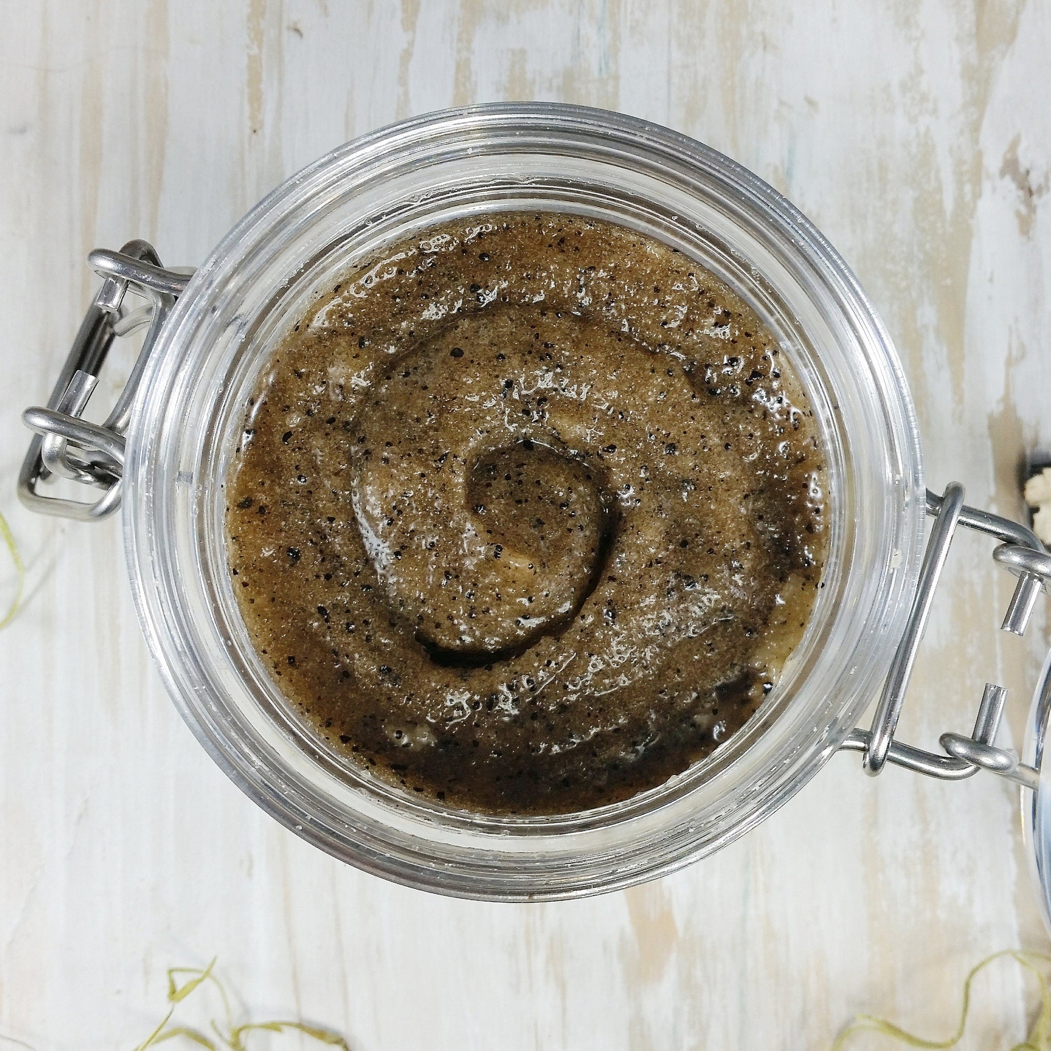 Body scrub in a clear glass jar with brown granules and swirl pattern, metal clasp closure