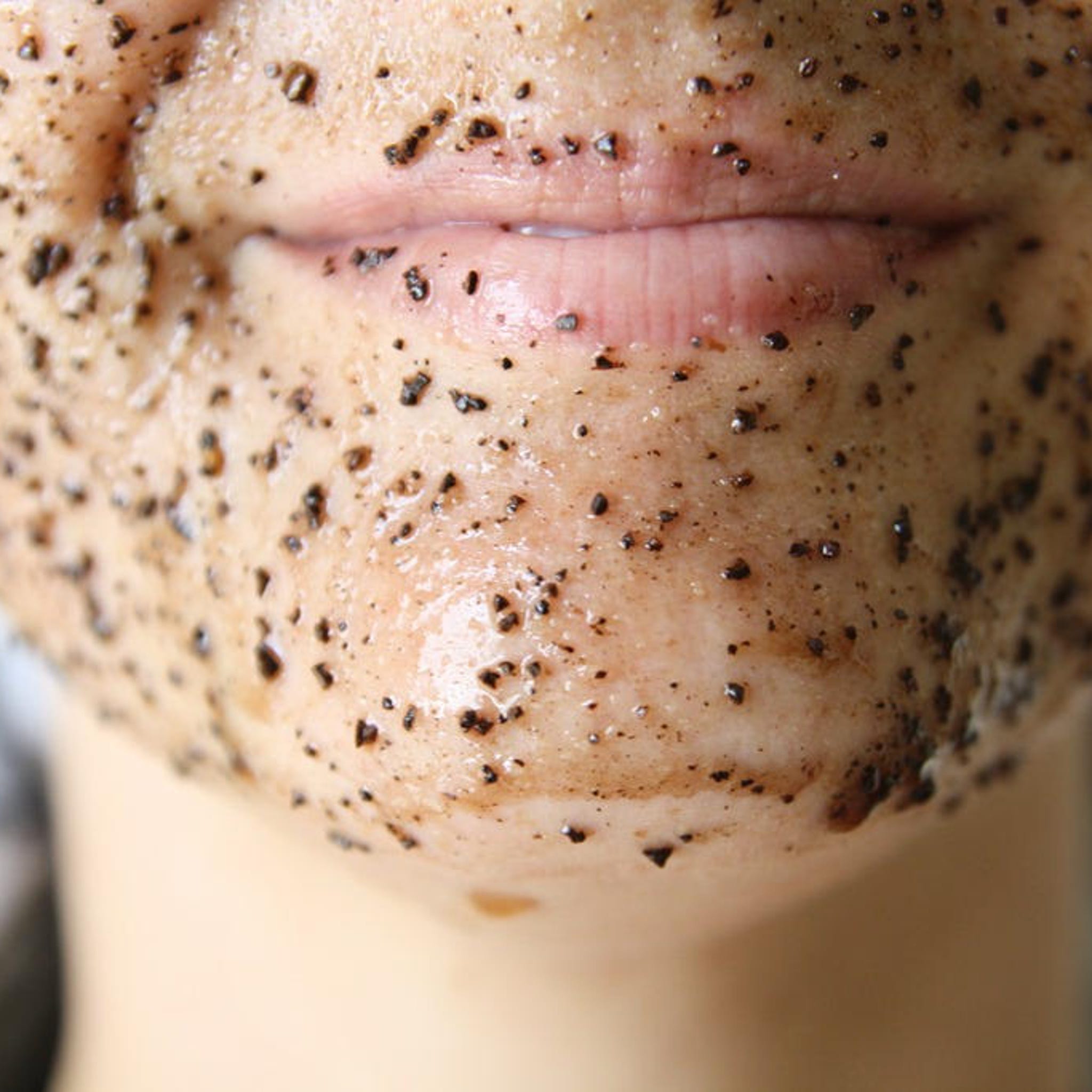 Facial scrub on skin with brown and black particles, close up of lips and face