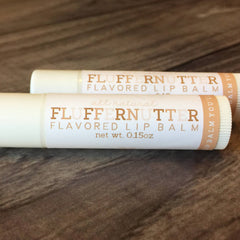 Lip balm tubes with white and tan labels, text "FLUFFERNUTTER FLAVORED LIP BALM" visible, on wooden surface