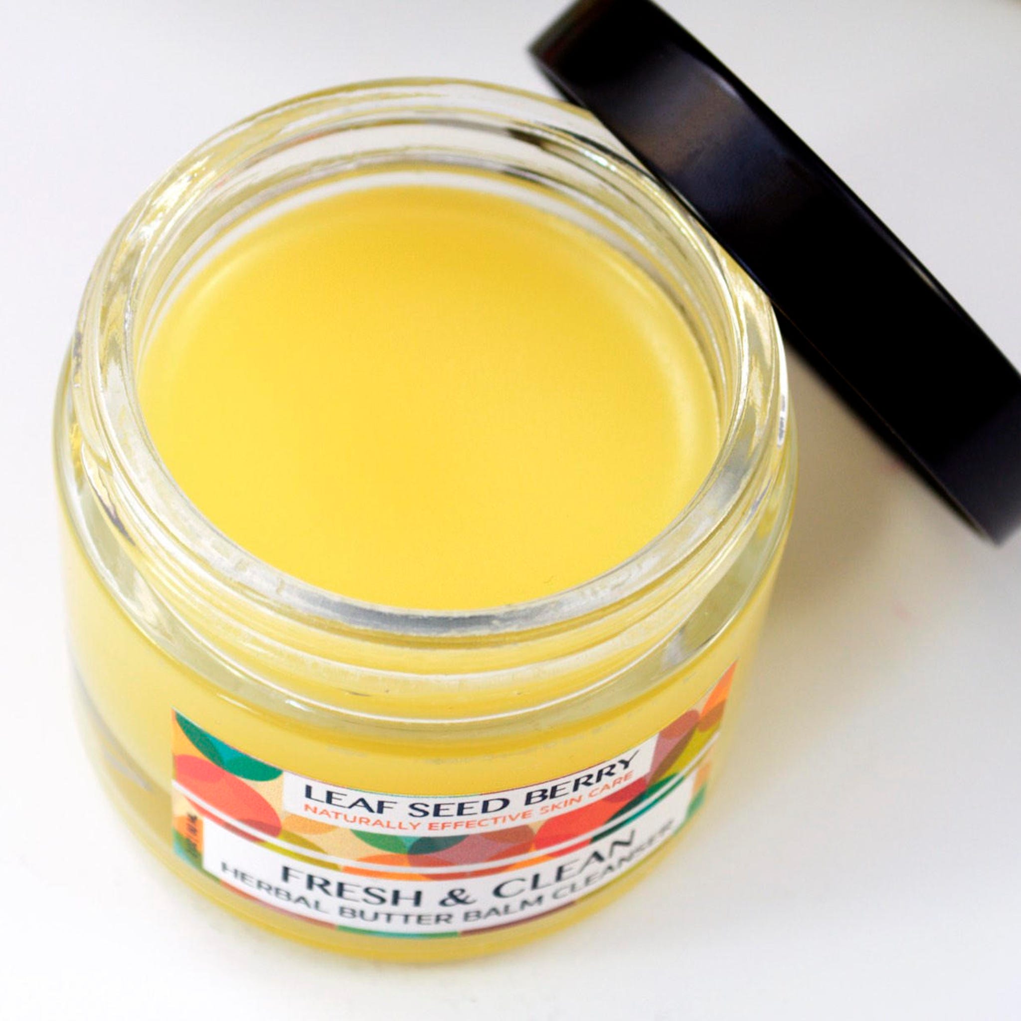 Herbal butter balm cleanser in glass jar with yellow balm, black lid, and label