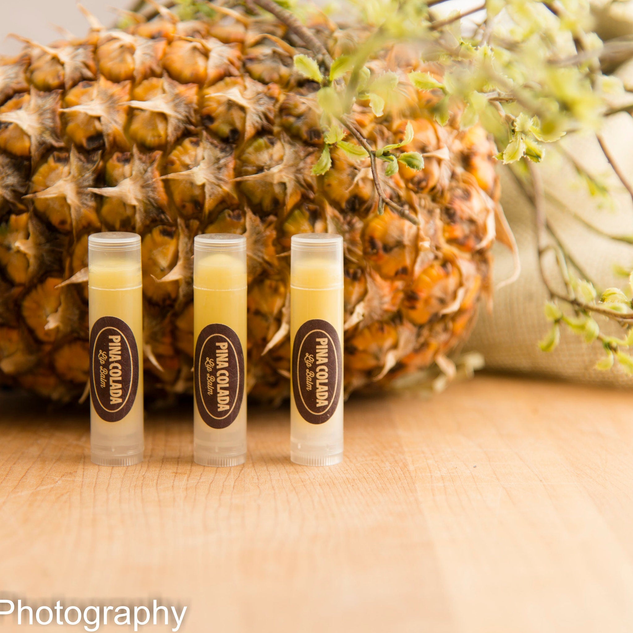 Lip balm tubes with "Pina Colada" label, yellow liquid, clear plastic, and pineapple background