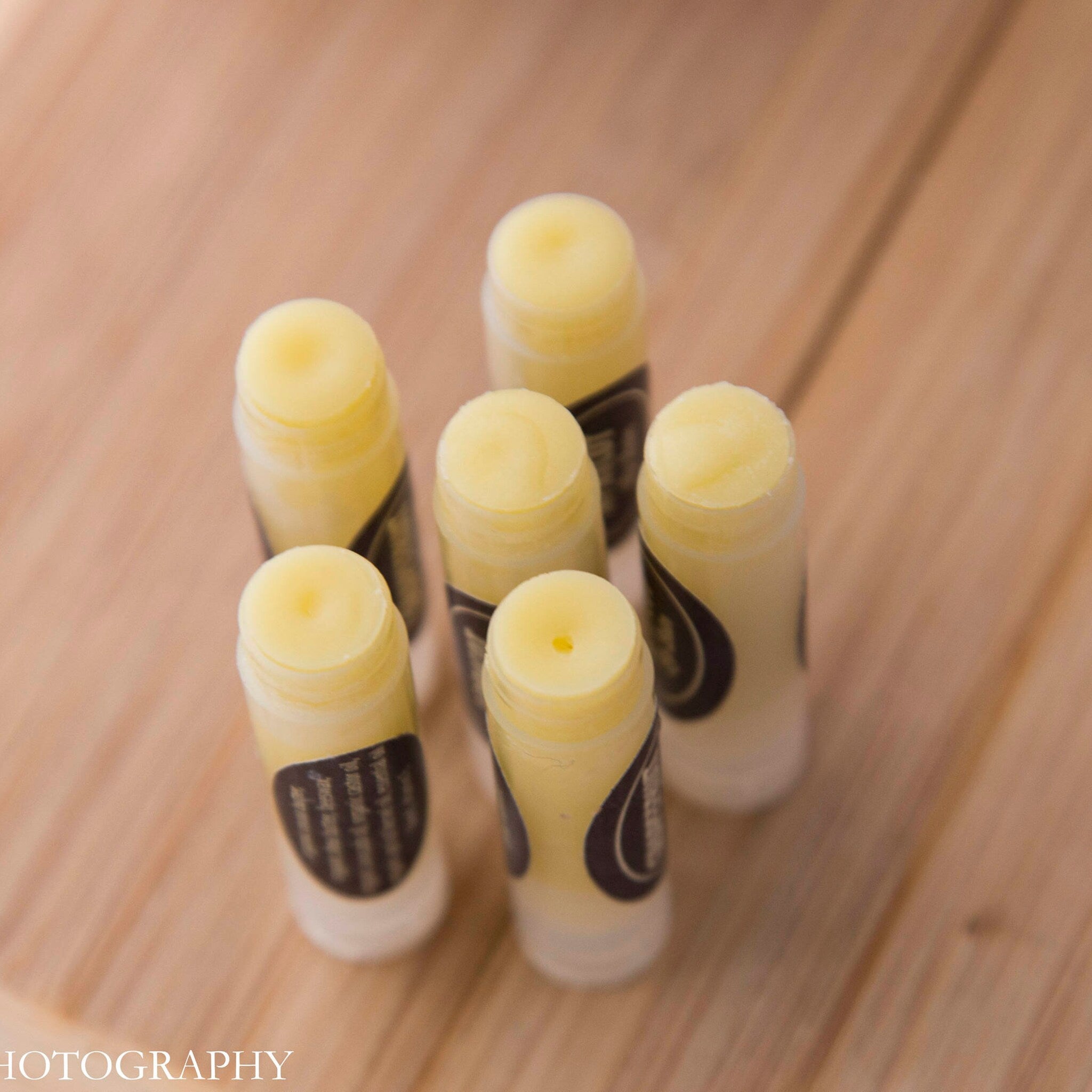 Lip balm tubes with yellow balm, white and brown labels, on a wooden surface