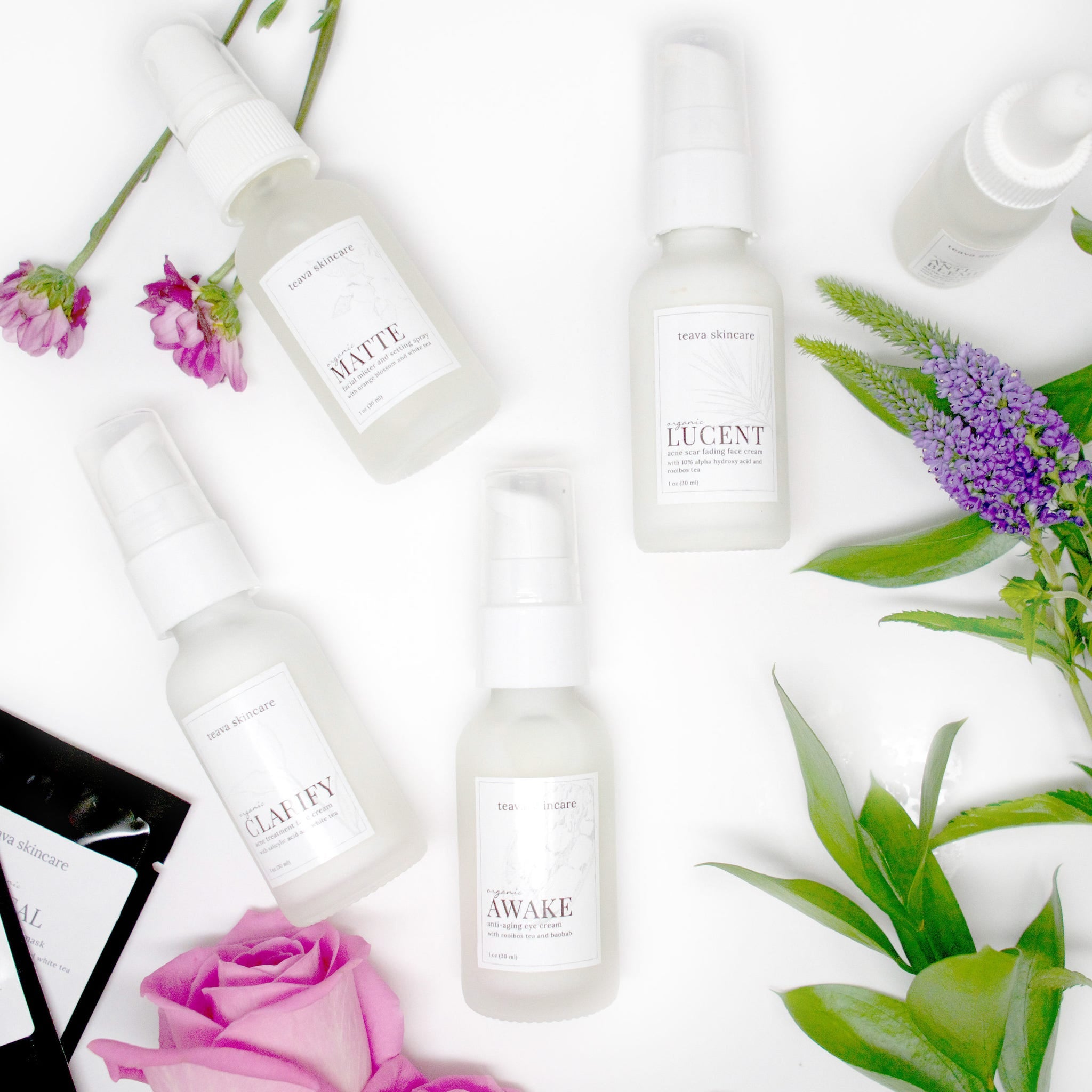 Skincare products with white bottles, white labels, and floral arrangement on white background.